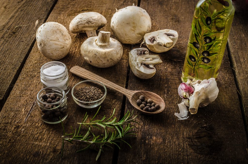 hampignons frais, herbes, épices et huile d'olive disposés sur une table en bois rustique