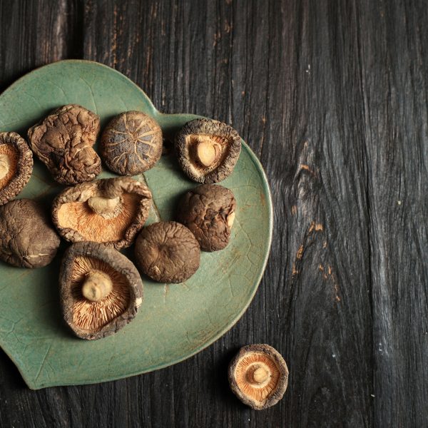 Champignons shiitake séchés disposés sur une assiette en forme de feuille, posée sur une table en bois sombre. Connus pour leurs effets bénéfiques sur la santé cardiovasculaire, les shiitakes aident à réduire le cholestérol et soutiennent le système immunitaire.