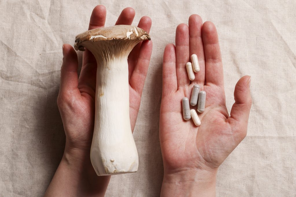 Champignon frais et compléments alimentaires naturels dans les mains, sur un fond en tissu beige.