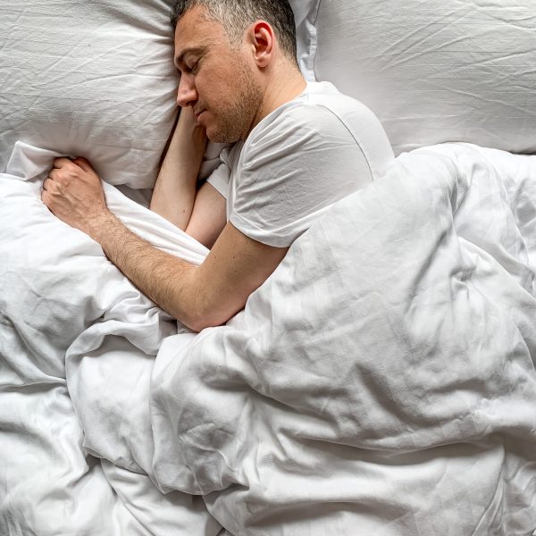 Homme dormant paisiblement dans un lit avec des draps blancs. Le champignon Reishi est reconnu pour ses effets apaisants et adaptogènes, favorisant un sommeil réparateur et réduisant le stress naturellement.